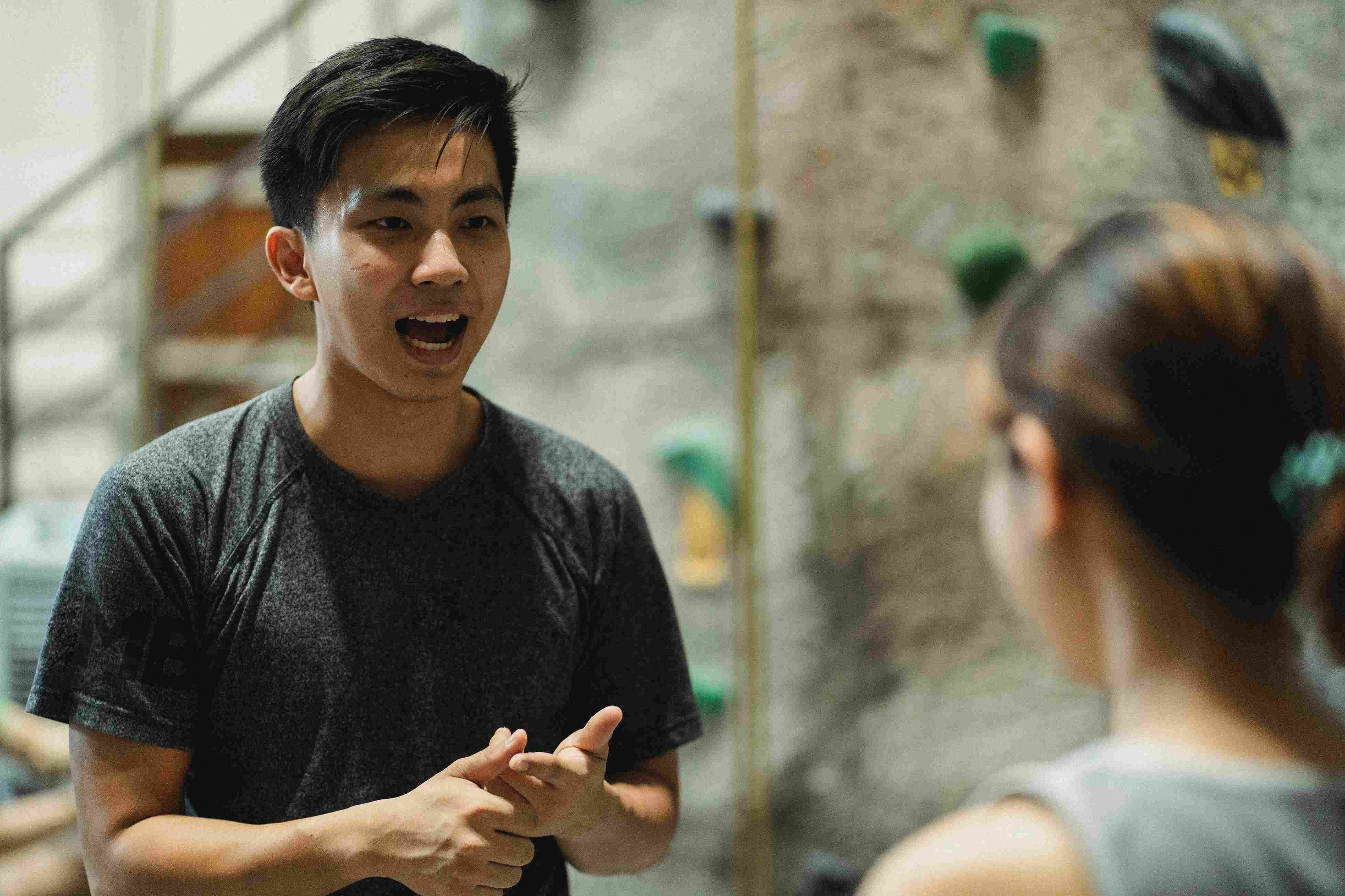 Asian male trainer speaking with unrecognizable climber before training